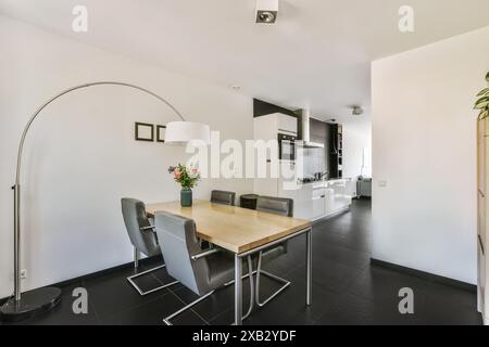 Elegant modern dining room seamlessly connected to a white and black kitchen, featuring a curved floor lamp and a flower arrangement in Oostzijde, Ams Stock Photo