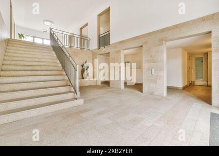 A bright and airy lobby in Amsterdam, featuring a wide stone staircase flanked by metal railings, large windows for natural light, and minimalist deco Stock Photo