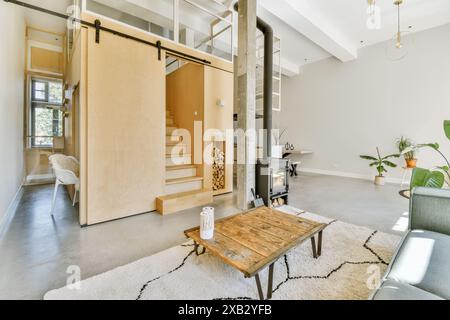 This photo showcases a modern living room interior with a wooden staircase, sliding door, concrete floor, and minimalist furniture. The natural light Stock Photo