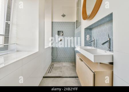 Elegant bathroom featuring blue hexagonal tiles, a sleek white countertop, and warm wooden details, accentuated by natural light. Stock Photo