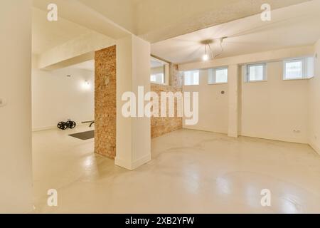 Empty basement interior showcasing a large room with polished concrete floor, exposed brick column, and white walls with light fixtures and small wind Stock Photo