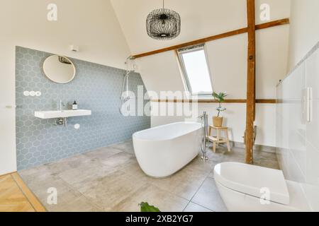 Contemporary bathroom featuring a white freestanding bathtub, geometric tile wall, and skylight, blending luxury with rustic wooden beams. Stock Photo