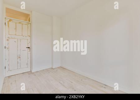 A minimalist interior showcasing an empty room with white walls and a wooden door, revealing weathered textures indicative of a vintage aesthetic Stock Photo