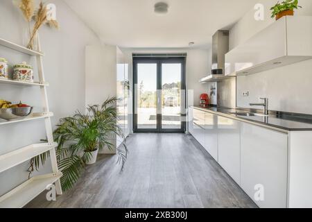 A view of a modern, well-lit kitchen with sleek white cabinetry and black countertops in a newly designed apartment The room features floor-to-ceiling Stock Photo