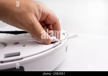 A person is fixing a white device with a red button. The device is a robot vacuum cleaner Stock Photo