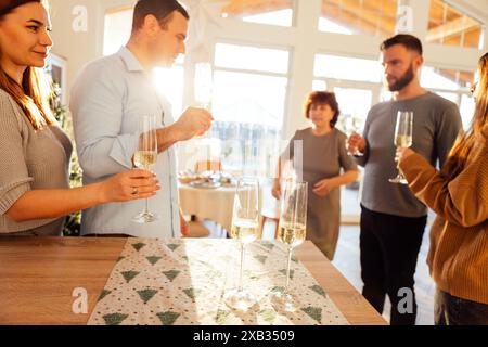 Smiling people raise glasses of champagne in dining room of house. Married couples of different ages celebrate Christmas Eve. Big happy family and fri Stock Photo