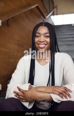 Happy young woman with braided hair sitting on staircase Stock Photo