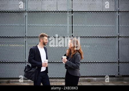 Mature male and female colleagues talking with each other while standing against grate wall Stock Photo