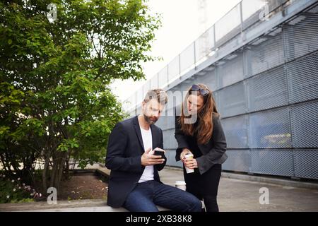 Businessman sharing smart phone with female colleague while sitting on bench at footpath Stock Photo