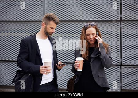 Businesswoman talking on smart phone by male colleague with disposable cup against grate wall Stock Photo