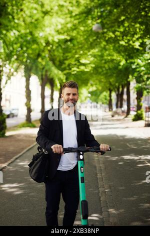 Smiling businessman with electric push scooter standing on footpath Stock Photo