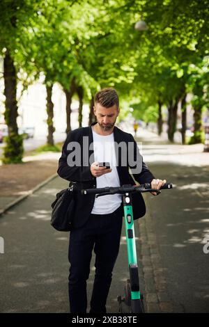 Businessman text messaging over smart phone while standing with electric push scooter on footpath Stock Photo
