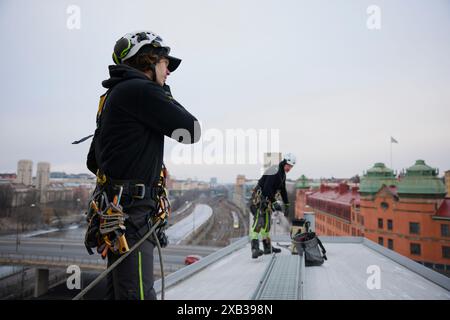 Male rope access workers in protective workwear standing on rooftop Stock Photo