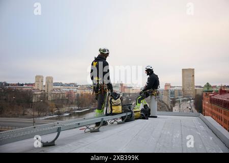 Male rope access workers in protective workwear with bags on rooftop of building Stock Photo