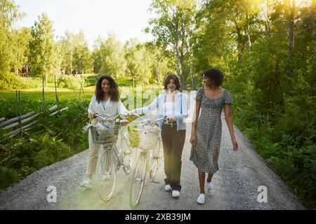 Happy young friends walking with bicycle on road Stock Photo