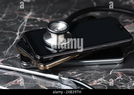 Stack of modern smartphones and stethoscope on black table Stock Photo