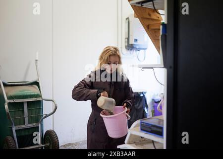 Female farmer with pouring dirt in bucket while standing at stable Stock Photo