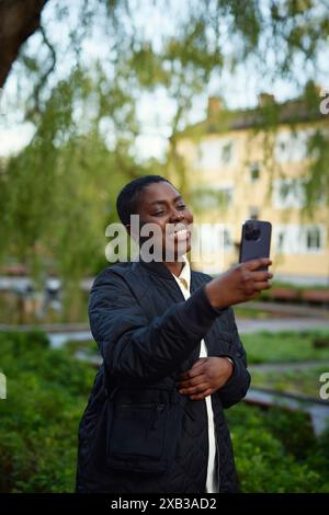 Happy mature woman taking selfie on smart phone standing in park Stock Photo