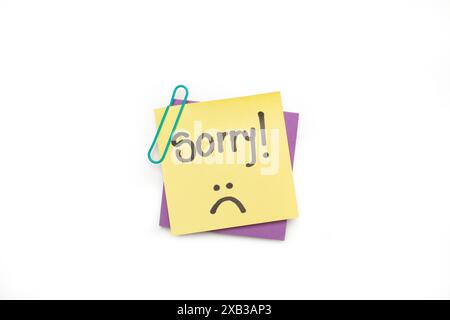Sorry word and a sad face on a yellow sticky paper on a white background Stock Photo