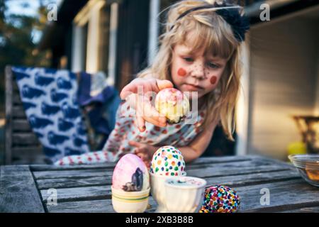 Girl putting colorful Easter eggs in containers on table Stock Photo
