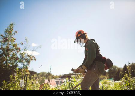 Woman with weed trimmer in back yard against sky on sunny day Stock Photo