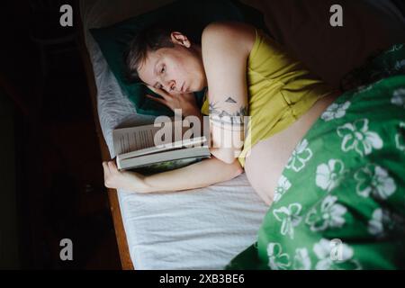 High angle view of pregnant woman reading book while lying in bed Stock Photo