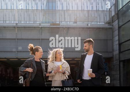 Female and male colleagues with disposable cups discussing while standing at subway station Stock Photo