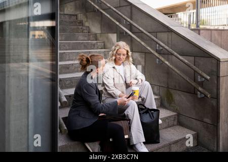 Female business colleagues discussing with each other while sitting on steps Stock Photo