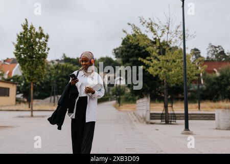 Smiling woman using smart phone while walking on footpath Stock Photo