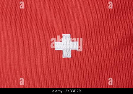 white hospital plus or medical cross sign on red textured fabric surface background, embroidered swiss national flag with copy space Stock Photo