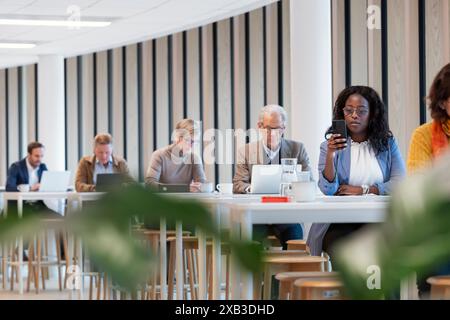 Businesswoman using smart phone while sitting at table in office cafeteria Stock Photo