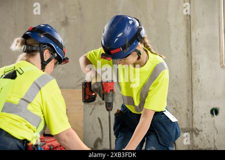 Female engineer using drill while working with coworker at construction site Stock Photo