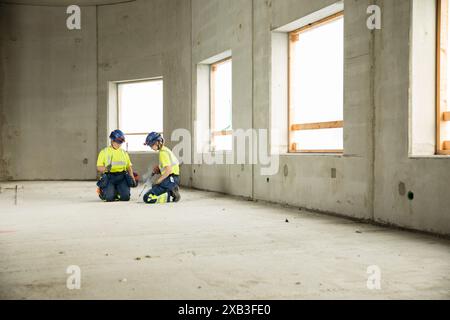 Female engineers kneeling and using equipment while working at construction site Stock Photo
