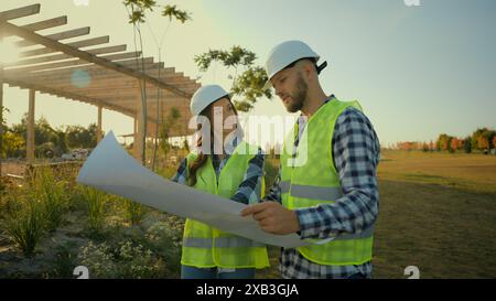 Two Caucasian happy professional engineers smiling successful builders contractor woman female girl man guy helmet male workers talking discuss Stock Photo