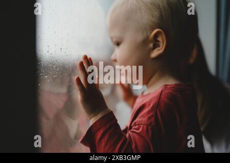 Side view of cute blond boy looking out through from window at home Stock Photo