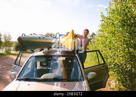 Woman putting kayak on car hood during vacation Stock Photo