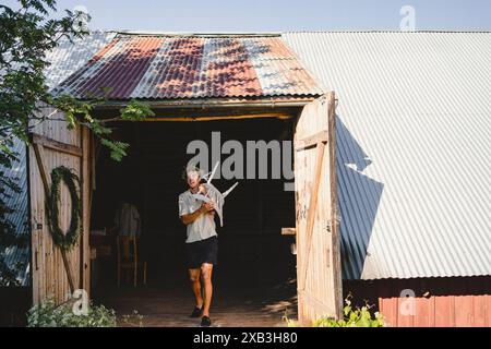 Full length of young man carrying chair on shoulder while moving out from shed Stock Photo