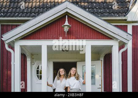 Portrait of happy young female friends standing at front door Stock Photo