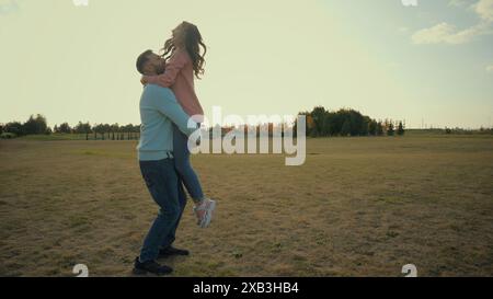 Young laughing Caucasian lovers couple woman female lady spouse running jumping male man guy arms catch spin around hug cuddle whirl happy family Stock Photo