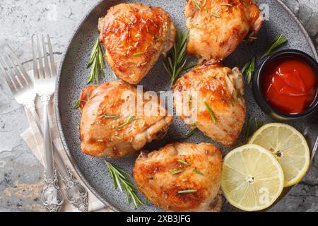 Delicious homemade Lemon rosemary chicken thighs served with ketchup close-up in a plate on the table. Horizontal top view from above Stock Photo