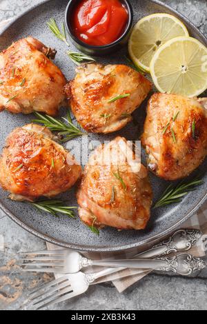 Traditional baked chicken thighs with lemon and rosemary served with tomato sauce close-up in a plate on the table. Vertical top view from above Stock Photo