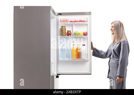 Young woman in pajamas opening a fridge in the middle of the night isolated on white background Stock Photo