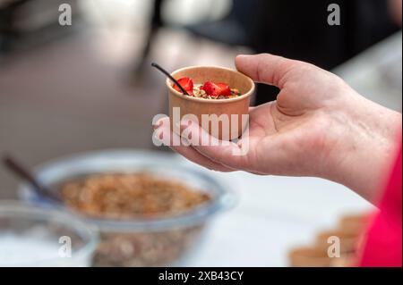 A close-up shot of a hand holding a small bowl of granola and strawberries. Stock Photo