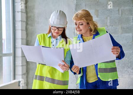 Two female industrial workers with technical plan at construction site Stock Photo