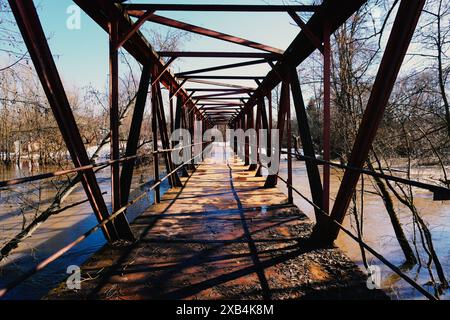 Old rusty bridge made of metal trusses over a dirty river Stock Photo