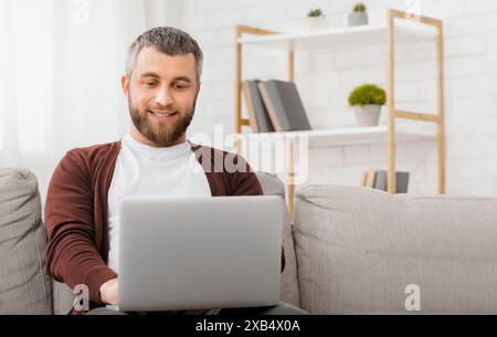 Cheerful Man Sitting on Couch Using Laptop Stock Photo
