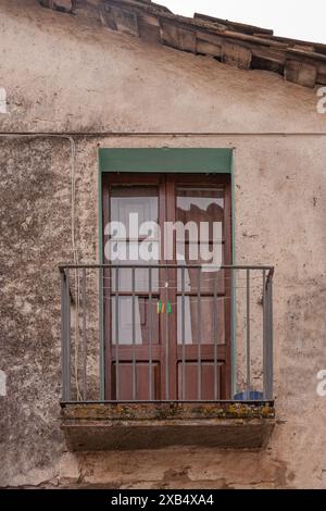 An exterior old iron balcony with cantilever. It has a wooden window and a small rope with clothespins to hang clothes on. Stock Photo