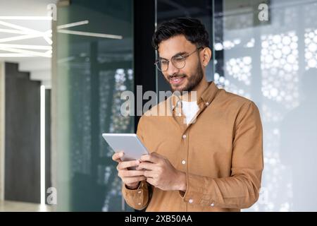 Young smiling Muslim male programmer and designer standing in modern office and using tablet. Stock Photo