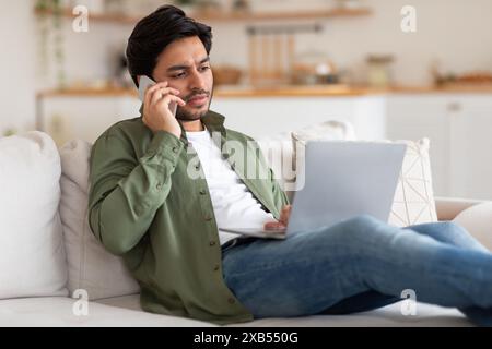 Man Talking On Phone While Working On Laptop From Home Stock Photo