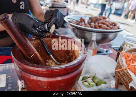 A close-up view of a person wearing black gloves using a wooden mortar and pestle to prepare traditional Thai papaya salad, also known as Som Tum. Stock Photo